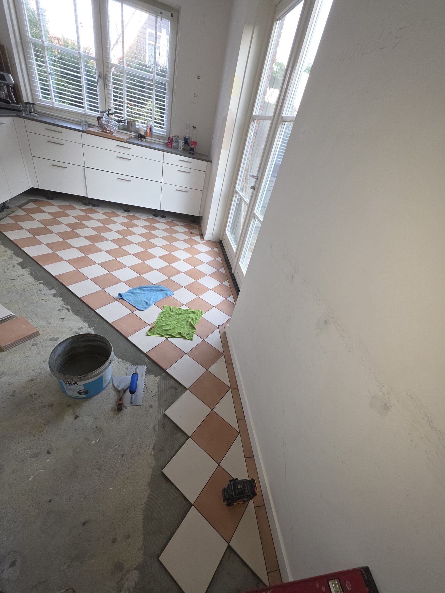 Half afgeronde tegelvloer tijdens het leggen, met lijmemmer en troffels