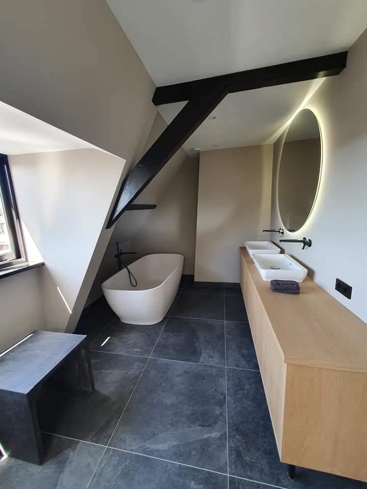 Badkamer met ligbad, houten wastafelmeubel en donkere vloertegels